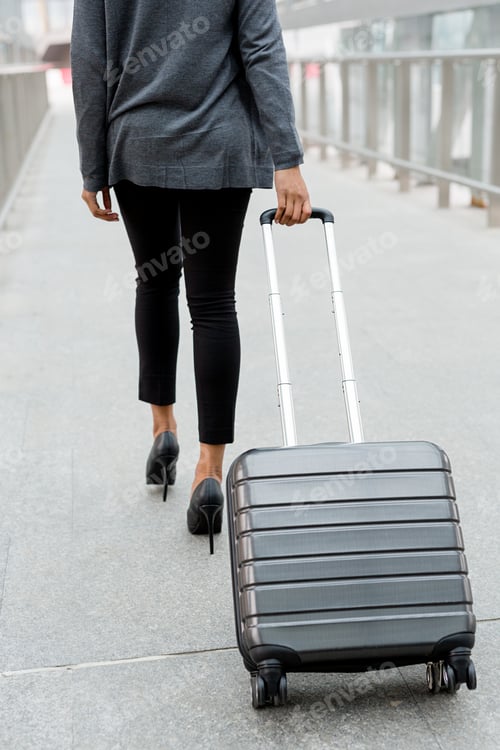 Preview: Unrecognizable businesswoman pulling suitcase inside of airport terminal