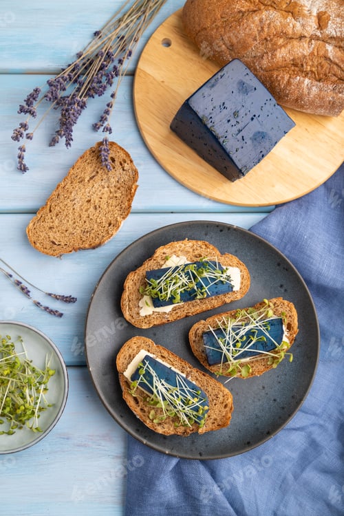 Preview: Bread sandwiches with blue lavender cheese and mustard microgreen on blue, top view, close up.
