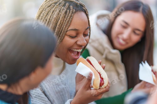 Preview: African woman eating hot dog with friends in a park
