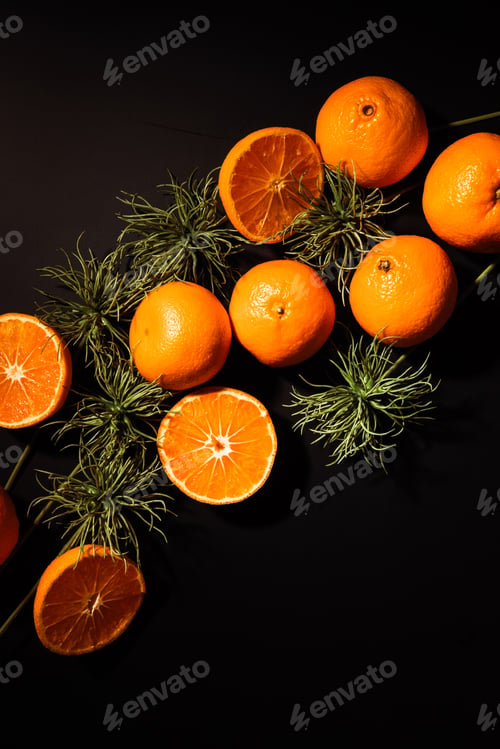 Preview: top view of fresh tangerines and green plants arranged on black tabletop