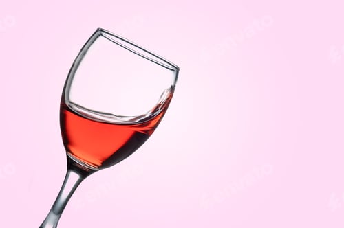 Preview: Tilted wineglass with rose wine splashing on pink background