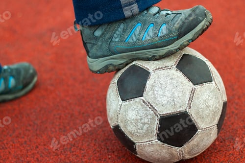 Preview: Human foot in a dirty sneaker on an old soccer ball