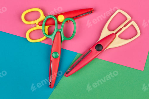 Preview: Three colorful scissors on color paper background.