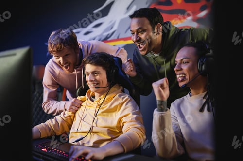 Preview: Excited interracial men looking at friend playing video game on computer in gaming club