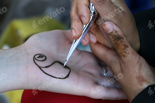 Preview: Henna artist creating design on palm of hand.