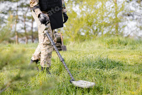 Preview: A man in a military uniform and bulletproof vest works in the forest with a metal detector