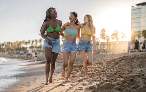 Preview: three multiracial female friends walking on the sand of the beach happy at sunset