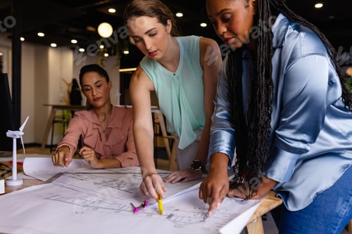 Preview: Diverse female architects in discussion using blueprints in casual office meeting