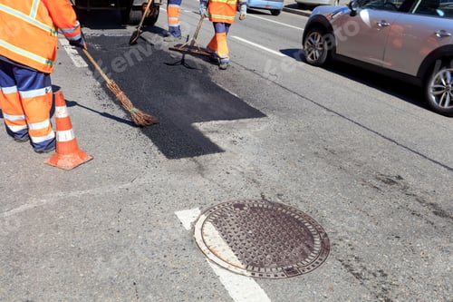 Preview: Closeup shot of road workers near a manhole repairing part of the road with fresh hot asphalt