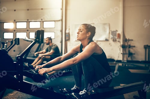 Preview: Two fit people exercising on rowing machines at the gym