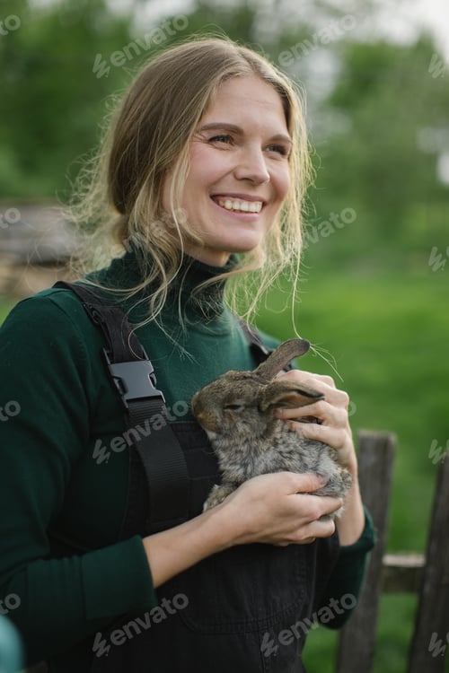 Preview: A happy blonde woman holds a rabbit in her arms. Aesthetics of rural life.