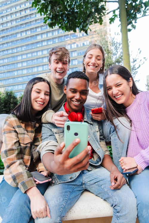 Preview: Vertical. Multiracial group of friends enjoying and smiling using a cellphone app. Diverse teenagers