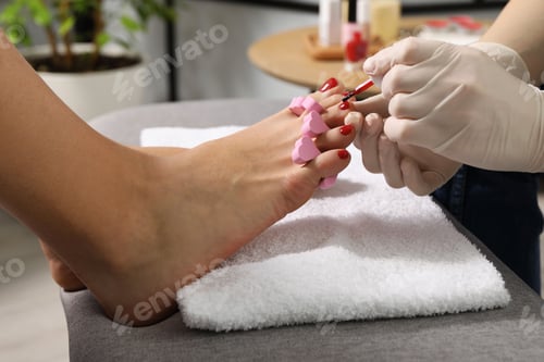 Preview: Pedicurist painting client`s toenails with red polish in beauty salon, closeup