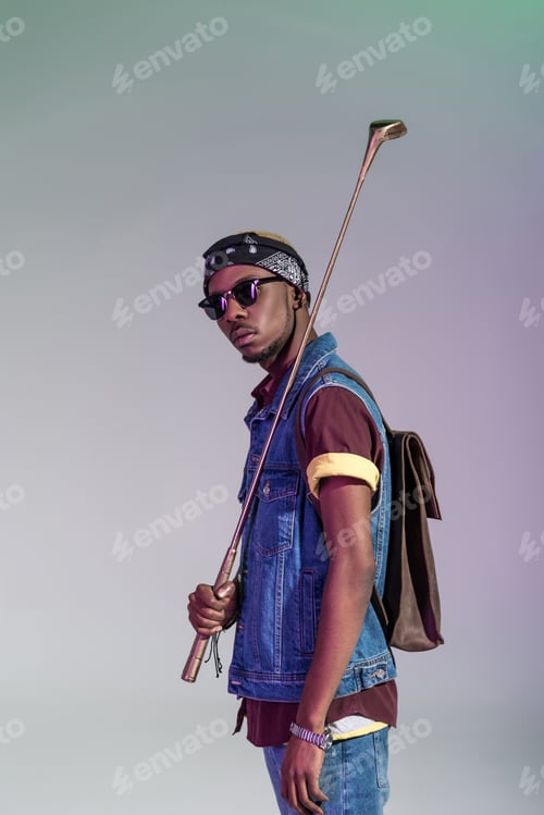 Preview: stylish young african american man holding golden golf club and looking at camera isolated on grey
