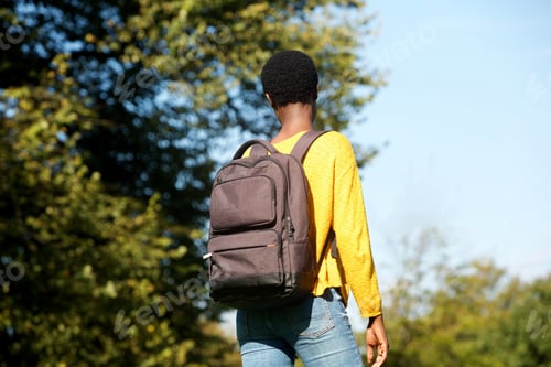 Preview: behind of young black woman walking in park with bag