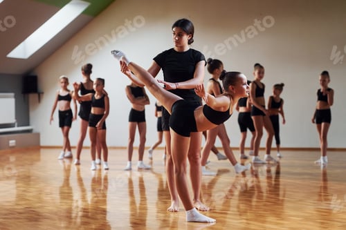 Preview: Woman teaching and helping. Group of female kids practicing athletic exercises together indoors
