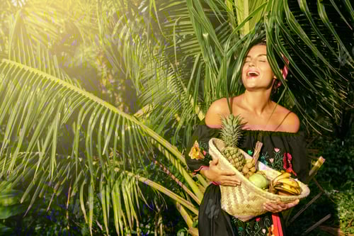 Preview: Happy young woman with a basket full of exotic fruits