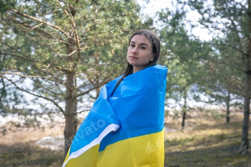 Preview: A young woman wrapped in the flag of Ukraine on a blurred background.