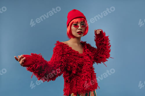 Preview: Charming cool woman with red wig, sunglasses and bright makeup in long sleeve warm sweater and cap