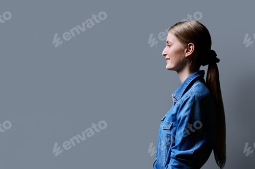 Preview: Profile view, young smiling female looking forward on gray studio background