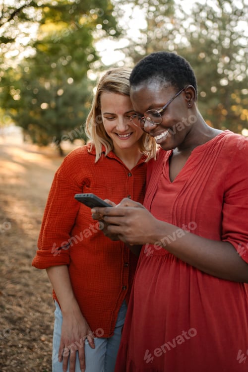 Preview: Two smiling friends looking at smartphone in a park