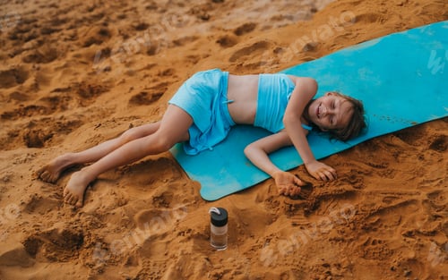 Preview: Child Rests on Blue Yoga Mat at Beach