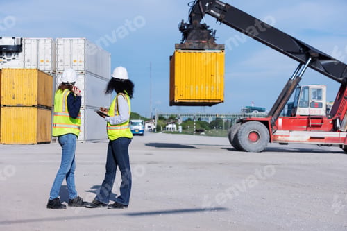 Preview: Two female engineers in safety vests and helmets oversee container handling at a shipping yard.