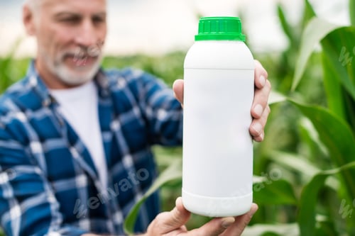 Preview: Closeup a bottle with chemical fertilizers in the hand's of middle aged farmer standing in a field.