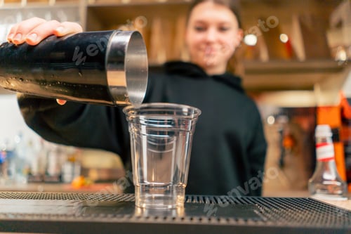 Preview: a young girl in an establishment behind the bar pours ice from shaker into a plastic glass