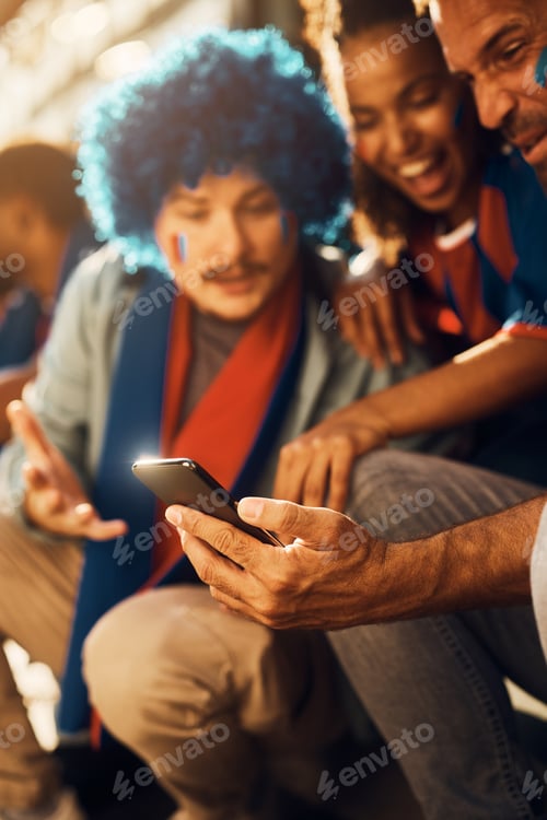 Preview: Close up of soccer fans watching live match broadcast on mobile phone.