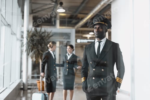 Preview: thoughtful young pilot in airport with stewardesses before flight