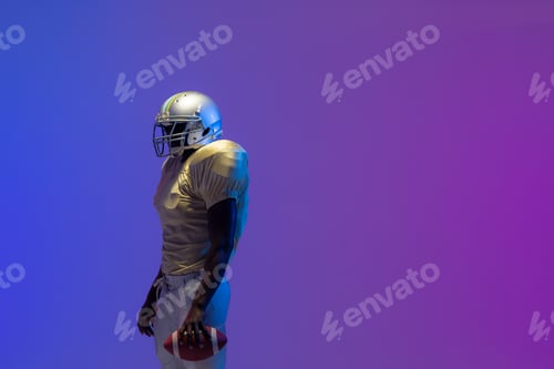 Preview: African american male american football player holding ball with neon blue lighting