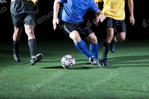 Vista previa: Soccer players competing for the ball on a green turf field at night