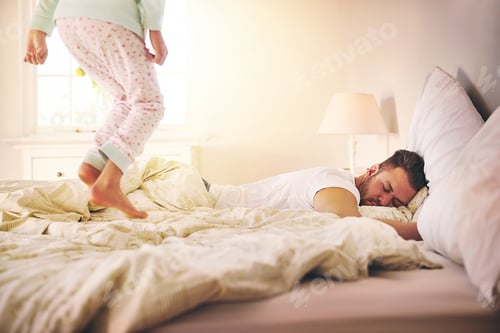 Preview: Shot of a cheerful little girl jumping on the bed to wakeup her sleeping dad at home