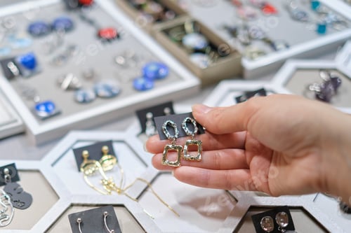 Preview: customer's hand reaches for an artisanal earring at a market stand, where an assortment of handmade