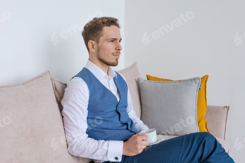 Preview: Businessman in blue suit sitting in his office sofa sits with coffee cup