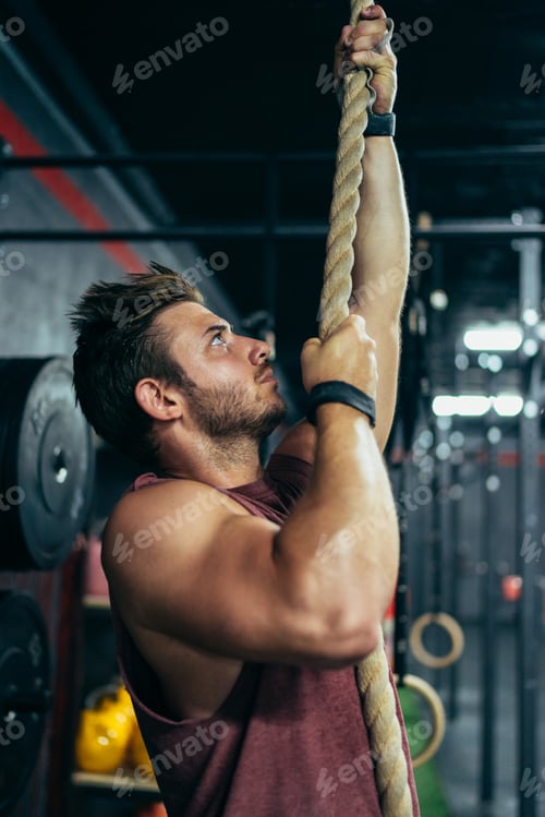 Preview: Vertical photo of a strong man climbing a rope in a gym