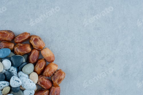 Preview: Brown dry dates on blue background with colorful beach stones around