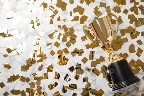 Preview: Gold trophy cup and confetti on marble background, flat lay. Space for text