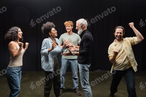 Preview: tattooed producer talking to happy african american woman near excited multiethnic actors.
