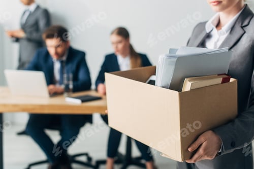 Preview: Selective focus of fired woman holding cardboard box with book and papers in office