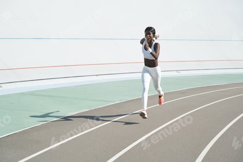 Preview: Beautiful young African woman in sports clothing running on track outdoors