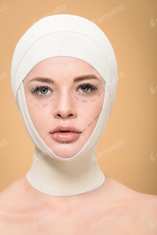 Preview: young woman with bandages over head and lines on face looking at camera isolated on beige