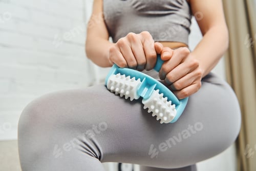 Preview: Close up view of young blurred woman in sportswear massaging leg with handled massager while
