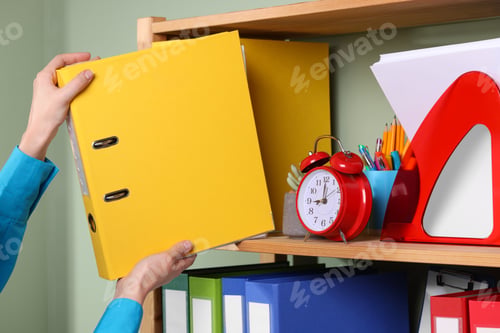 Preview: Woman taking binder office folder from shelving unit indoors, closeup
