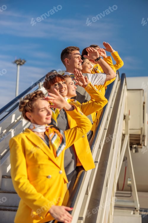 Preview: Cheerful airline workers standing on airplane stairs under blue sky