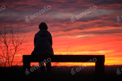 Preview: Dark silhouette of a lonely woman enjoying sunset view in evening nature.