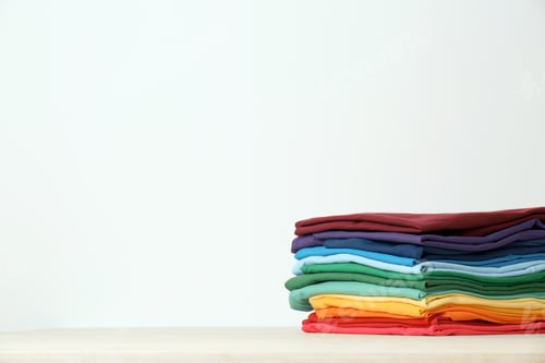 Preview: Stack of bright folded clothes on table against white background. Space for text