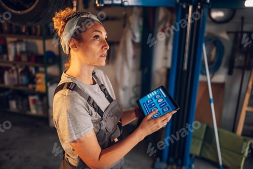 Preview: Female mechanic shop worker with tablet doing car diagnostics under chassis