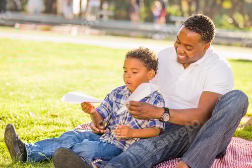 Preview: Happy African American Father and Mixed Race Son Playing with Paper Airplanes in the Park